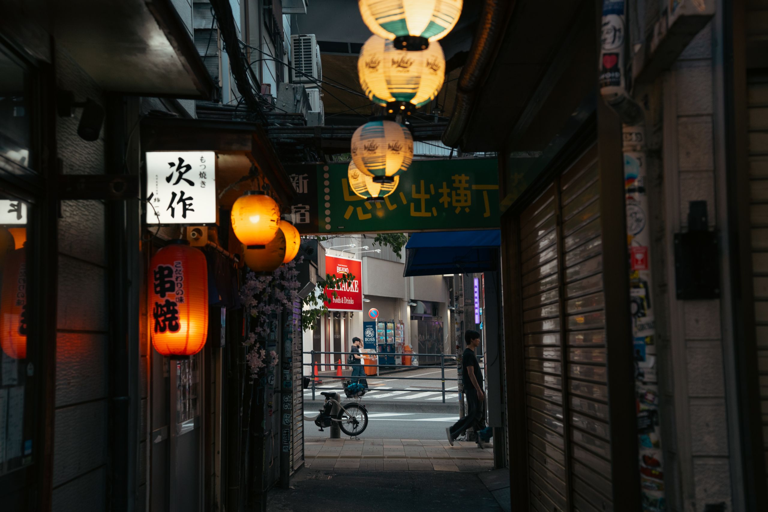 A narrow alley at night, paper lanterns lit above the doorways