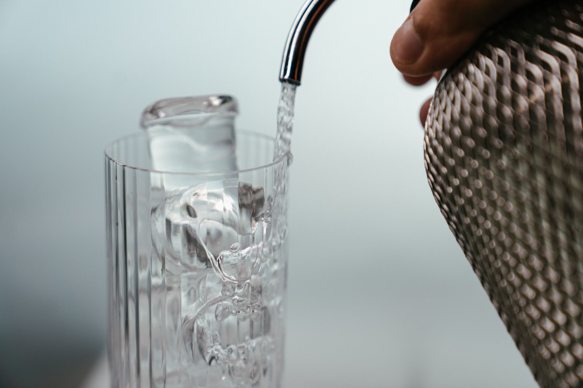 A clear drink being poured into a highball glass over ice